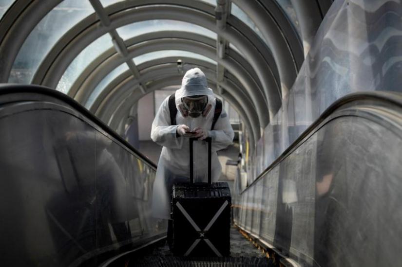 FILE PHOTO: A traveller wearing protective clothing and a full-face mask goes up an escalator after leaving Beijing Railway Station as the country is hit by an outbreak of the novel coronavirus disease (COVID-19), China, Mar 20, 2020. REUTERS
