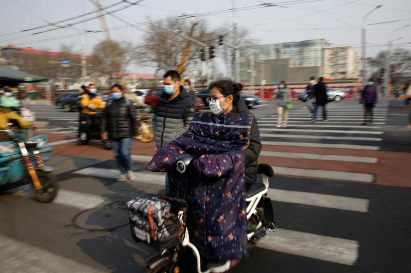 People wearing face masks ride their scooters and walk on a street following an outbreak of the coronavirus disease (COVID-19), in Beijing, China Mar 30, 2020. REUTERS